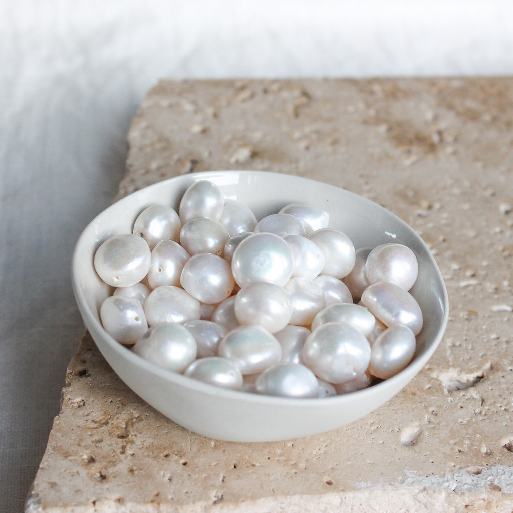 pearls in a bowl sitting on top of a travertine tile