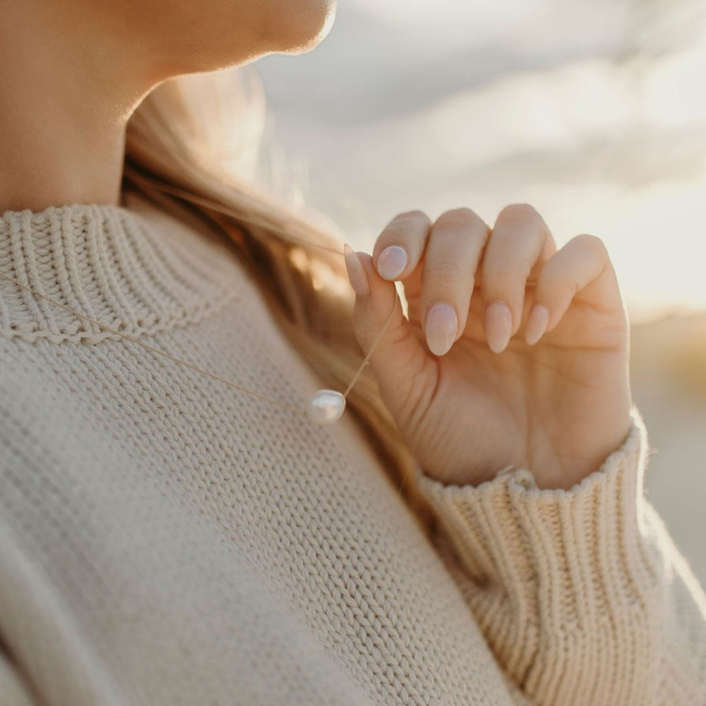 a person wearing a knit jumper holding a fine pearl chain necklace